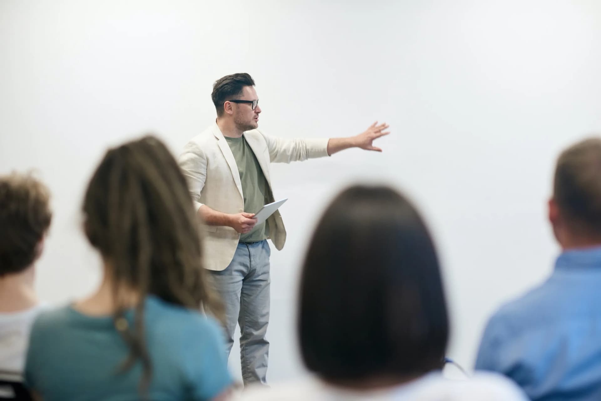 A speaker addressing a seated audience, gesturing towards a whiteboard
